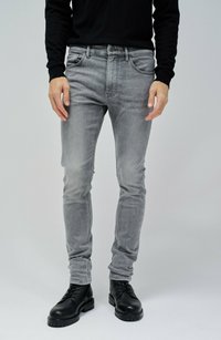Jeans de mezclilla gris con un ajuste slim, diseño de cinco bolsillos y un leve desgaste, combinados con botas negras de cordones y una camisa negra de manga larga.