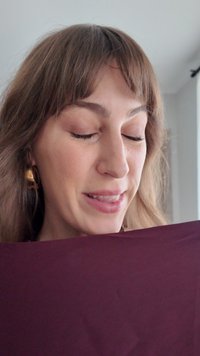 Burgundy fabric draped over hands, smooth texture, with a subtle sheen. Model has closed eyes and is positioned slightly to the side.