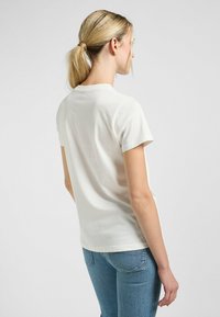 Witte katoenen t-shirt met korte mouwen, geribbelde ronde hals en een ontspannen pasvorm. Zichtbare stiksels langs de zoom en de schoudernaden.