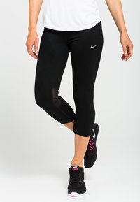 Czarne legginsy capri z siateczkowymi panelami, materiał odprowadzający wilgoć oraz małe, odblaskowe logo. Połączone z czarnymi sneakersami z różowymi akcentami.