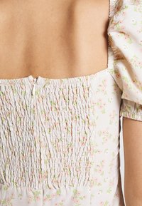 Robe florale blanche avec un dos smocké, ornée de motifs roses et verts, à manches courtes bouffantes et fermeture éclair dissimulée.