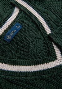 Maglione verde lavorato a maglia con strisce bianche lungo il colletto e l'orlo. Caratterizzato da motivi testurizzati e un'etichetta blu del marchio attaccata.