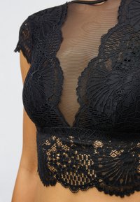 Čierny čipkovaný top s priesvitným sieťovaným živôtikom, krátkymi rukávmi a zložitými kvetinovými vzormi pozdĺž výstrihu a lemu.