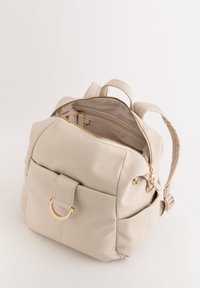 Mochila de cuero beige con superficie texturizada, herrajes en tono dorado, cremallera superior, bolsillo frontal con detalle en bucle y correas ajustables.