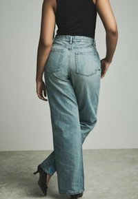 Lichtblauwe high-waisted jeans hebben een relaxte fit, zichtbare achterzakken en subtiele vervaging. Gecombineerd met zwarte hoge hakken.