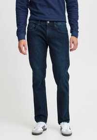 Mörkblå jeans i denim, rak passform med fem fickor, kombinerat med en marinblå tröja och vita sneakers med svarta detaljer.