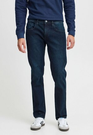 Mörkblå jeans i denim, rak passform med fem fickor, kombinerat med en marinblå tröja och vita sneakers med svarta detaljer.