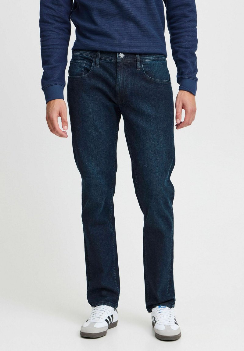 Mörkblå jeans i denim, rak passform med fem fickor, kombinerat med en marinblå tröja och vita sneakers med svarta detaljer.