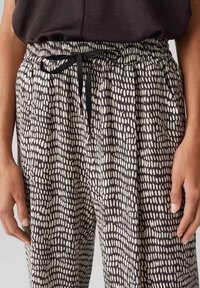 Pantalons extensibles avec une taille élastique et un cordon de serrage. Présente un motif de pois irrégulier noir et blanc et une texture de tissu douce.