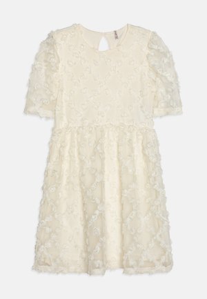 Robe crème avec des manches courtes bouffantes, texture florale et dos en cœur. Présente une jupe à volants avec une bordure en dentelle au niveau de l'ourlet.