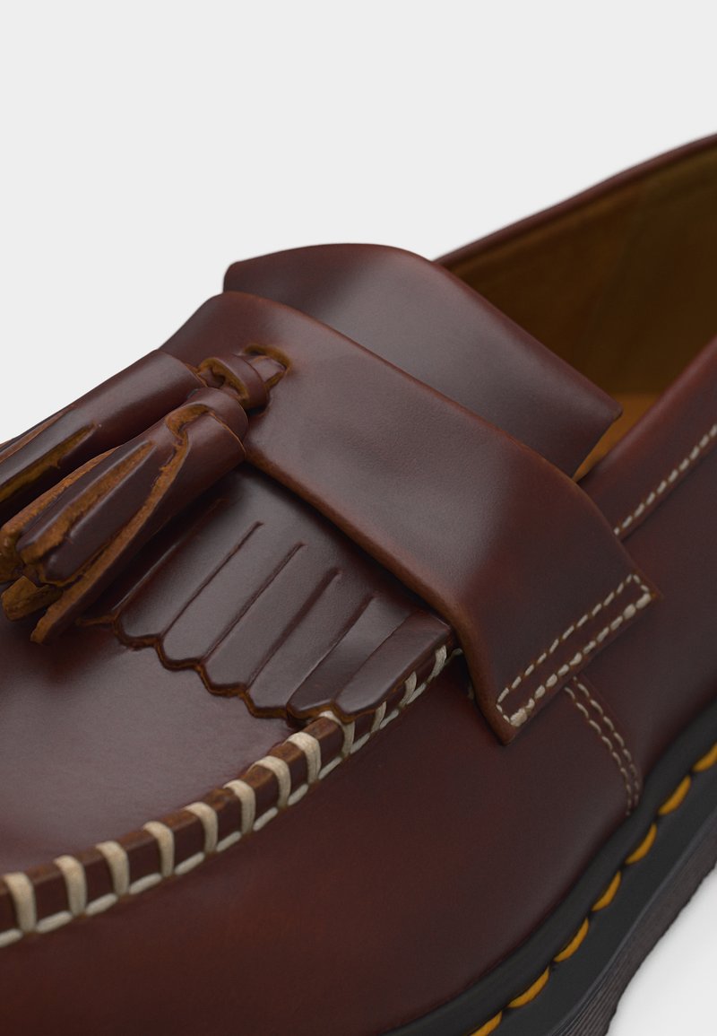 Mocassino in pelle marrone con nappine, cuciture a contrasto bianche lungo il bordo e suola nera con dettagli cuciti gialli.