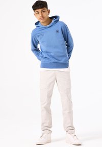 Lichtblauwe hoodie met bedrukt ontwerp, gecombineerd met crèmekleurige cargobroek en witte sneakers. De hoodie heeft een zachte textuur.