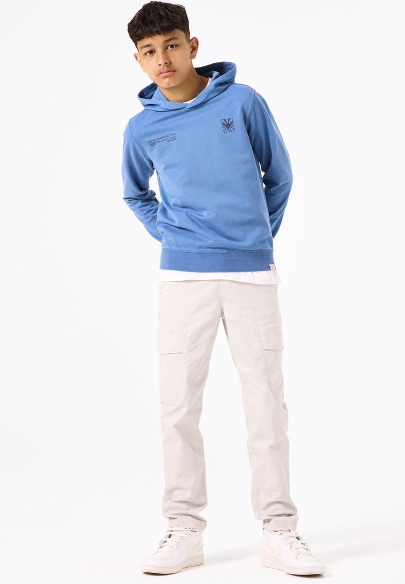 Lichtblauwe hoodie met bedrukt ontwerp, gecombineerd met crèmekleurige cargobroek en witte sneakers. De hoodie heeft een zachte textuur.