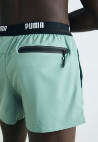 Világoszöld úszónadrág fekete gumis derékkal, melyen "PUMA" logó található, hátul zipzáros zsebbel.