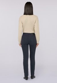 Beige kabelgebreide trui met lange mouwen, gecombineerd met donkergrijze slimfit broek. Zachte textuur en taps toelopend ontwerp. Zwarte taillebandaccent.