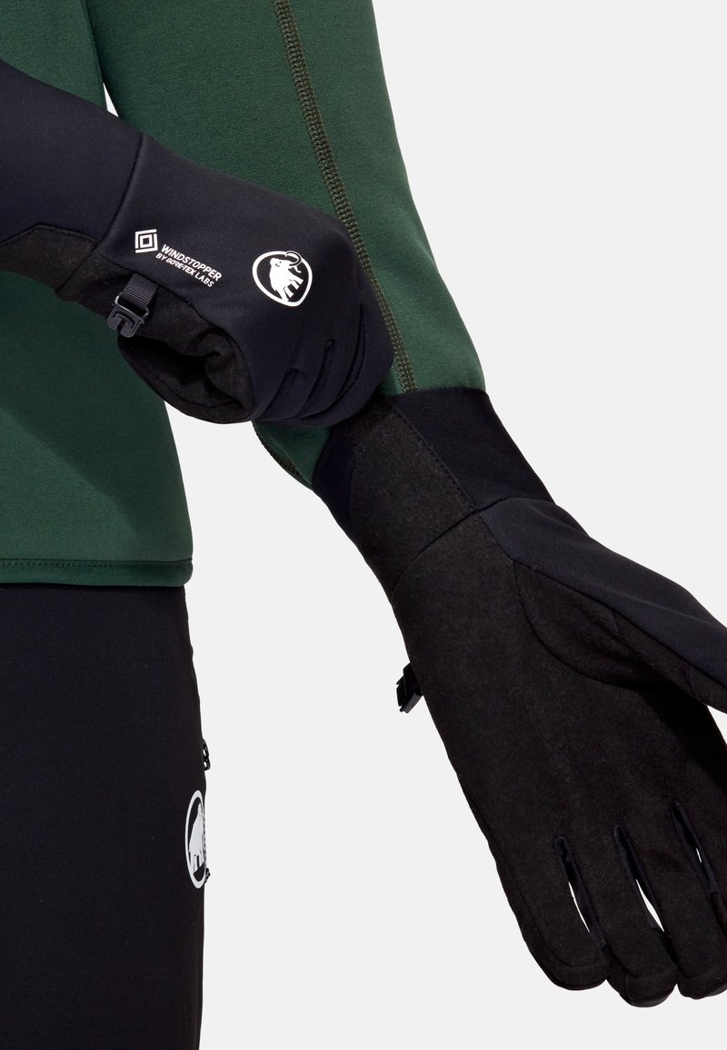 Black gloves with a fleece texture and windstopper feature. They have a fitted design and adjustable closure, shown with a green top.