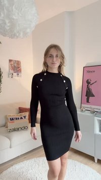 Melnā, ribota, garām piedurknēm, kleita ar pieguļošu siluetu, kas izceļas ar sudraba pogu akcentiem uz pleciem un augstu kaklu. Mīksta tekstūra.