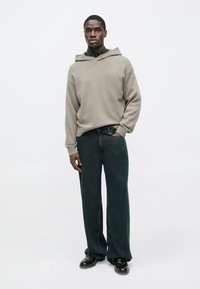 Grijze gebreide hoodie met een brede halslijn en geribbelde manchetten, gecombineerd met donkere denim broek met wijde pijpen en zwarte schoenen. Minimalistische designelementen.