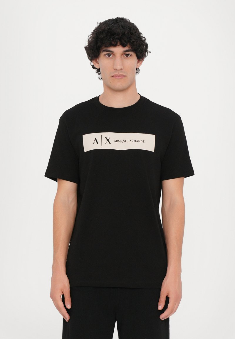 Svart bomull T-skjorte med korte ermer, med et kremfarget rektangulært logopanelsom viser "A/X ARMANI EXCHANGE" i svart skrift.
