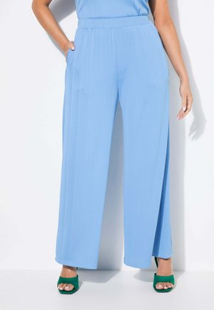 Pantaloni a gamba larga blu chiaro con tessuto testurizzato, caratterizzati da un'alta vita e tasche laterali. In abbinamento a tacchi aperti verdi.