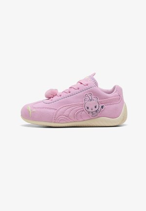 Roze suède kindersneaker met pomponveteraccent, cartoon buitenaards karakterpatch op de zijkant en lichtbeige zool.
