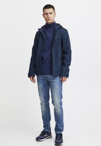 Jūras spēku mīksto apvalku ar rāvējslēdzēju, apvienojot ar jūras spēku krāsas augsto kaklu džemperi, gaiši ziliem džinsiem un melniem sporta apaviem.