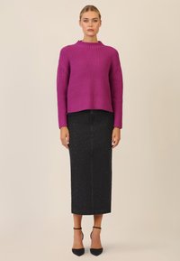 Maglione a coste magenta con collo alto, abbinato a una gonna midi in denim nera con dettagli sottili e tacchi a punta neri.