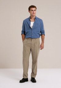 Gombos kék ing, fehér trikó, bézs pliszírozott nadrág és fekete cipő. Egyszerű dizájn, könnyű anyag és kényelmes szabás.