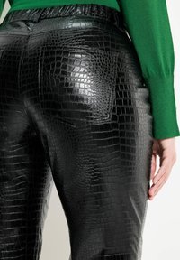 Pantalons en faux cuir noir avec un motif crocodile, dotés d'une taille haute et d'une ceinture élastique. Poches arrière visibles.