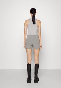Haut sans manches gris à col roulé côtelé associé à un short gris et des bottes noires jusqu'aux genoux. Fond blanc uni.