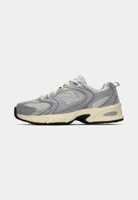 Chaussure de sport en maille grise avec une semelle extérieure crème, dotée d'un col rembourré, de lacets blancs et d'un logo subtil sur le côté. Accentuée de violet clair.