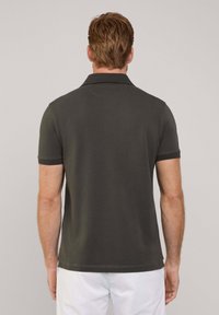 Czarny polo z klasycznym kołnierzykiem, krótkimi rękawami i miękką teksturą, pokazany od tyłu. Zawiera subtelne detale w szyciu.