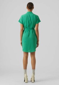Grön klänning med kort ärm som har en midja med bälte och en texturerad väv. Slutar ovanför knäet med en rak skärning och en krage.