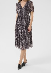 Robe midi à imprimé léopard avec un décolleté en V, des manches courtes et un design à volants. Fabriquée en tissu léger, elle a une texture fluide. Associée à des escarpins noirs à talons.