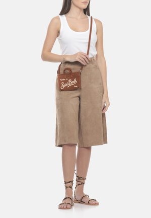 Donna con canotta bianca, gonna beige al ginocchio, sandali stringati con stampa leopardata e borsa a tracolla marrone con la scritta "Saint Barth".