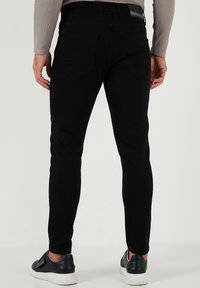 Svarta denimjeans med slim fit och bakfickor. Bärs med svarta sneakers som har vita sulor, vilket visar en elegant och modern design.