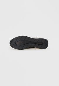 Semelle de chaussure en caoutchouc noir avec un motif de grip texturé ; présente le logo en relief "ALDO" près du centre et des lignes horizontales surélevées pour une traction accrue.
