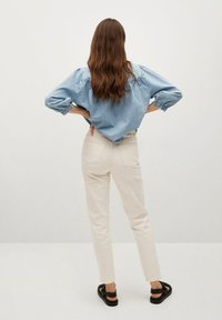 Vaaleansininen farkkupaita, jossa on puffihihat, yhdistettynä kermanvärisiin istuviin housuihin ja mustiin sandaaleihin, nähtynä takaa.