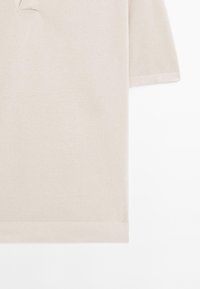 Pull en maille beige à manches courtes avec un col en V subtil et un ourlet et des poignets côtelés, présenté à plat sur fond blanc.