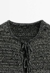 Czarny i biały sweter dzianinowy o fakturze, z okrągłym dekoltem i sznurkiem z przodu. Posiada różnorodne wzory tkane.