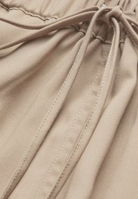 Pantalon en tissu beige avec taille élastique et cordon de serrage noué, montrant un gros plan sur la texture et les coutures.