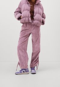 Puffig lavendelfärgad jacka med hög krage, kombinerad med matchande lavendelfärgade manchesterbyxor med cargo-fickor. Outfitten kompletteras med lila sneakers.