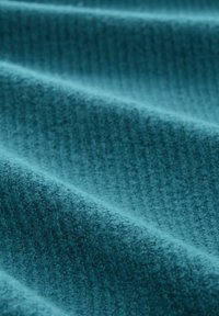 Gros plan sur un tissu teal texturé avec des plis doux et un motif tissé, mettant en valeur l'épaisseur du matériau et les détails de sa surface.