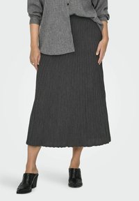 Gonna maxi grigia a costine con una texture morbida, caratterizzata da un orlo scallop. Abbinata a scarpe nere con tacco spesso e una camicia oversize con bottoni.