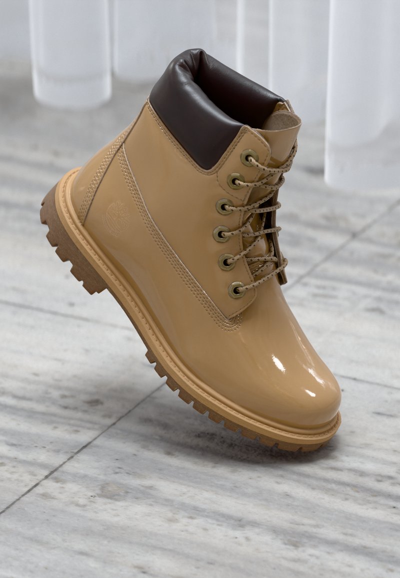 Stivale in pelle sintetica tan con un colletto imbottito marrone, occhielli in metallo dorato e suola in gomma strutturata. Presenta lacci robusti e un dettaglio del logo.