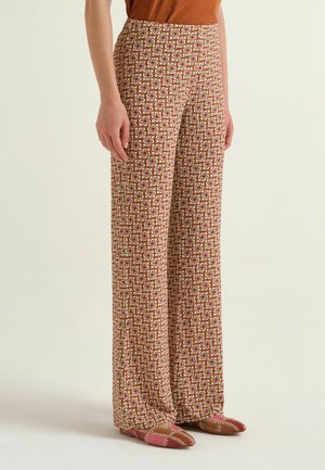 Femme portant un pantalon taille haute à jambes larges avec un motif géométrique multicolore et des chaussures plates pointues assorties.