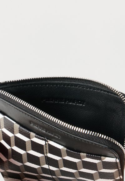 Μαύρο και άσπρο πορτοφόλι με γεωμετρικό σχέδιο και ανοικτό ασημί φερμουάρ που αποκαλύπτει το μαύρο δερμάτινο εσωτερικό και το ανάγλυφο όνομα της μάρκας.