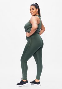 Olijfgroene sporttop en leggings gemaakt van rekbaar materiaal, met een aansluitend design, aangevuld met zwarte sportschoenen.