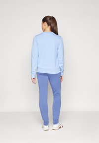 Svetlo modrý sveter s rebrovanými manžetami, skombinovaný s modrými teplákmi s elastickými manžetami na členkoch. Biely športový obuv dotvára outfit.