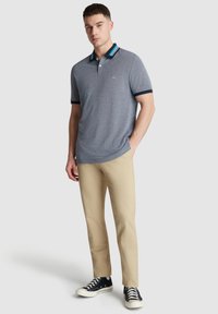 Polo shirt gris à manches courtes avec un col rayé bleu marine et teal, associé à un pantalon beige et des baskets bleu marine, présentant une tenue décontractée.